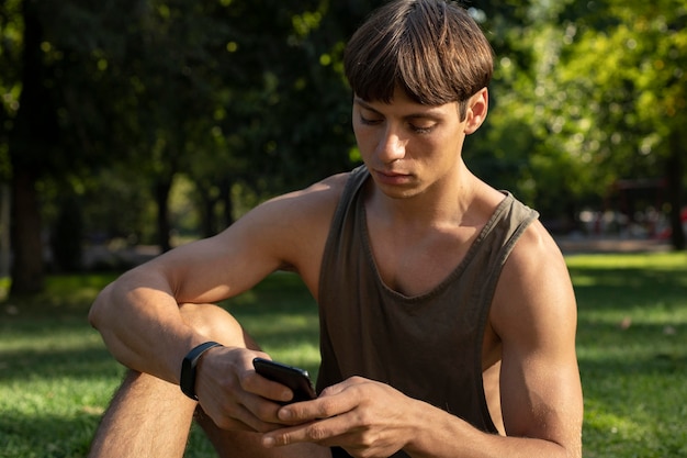 Homme en débardeur regardant smartphone tout en travaillant à l'extérieur