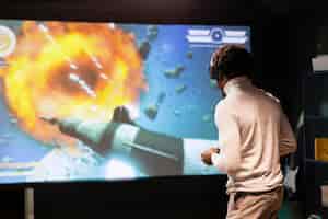 Photo gratuite un homme debout devant un écran ultra-large jouant à un jeu vidéo à l'aide d'un contrôleur