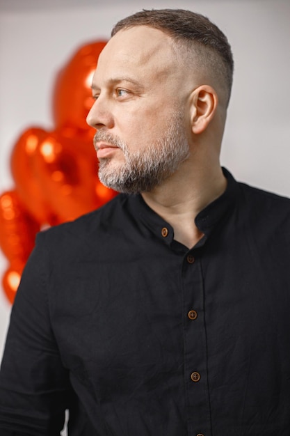 Homme debout devant un tas de ballons rouges en forme de coeur posant en studio