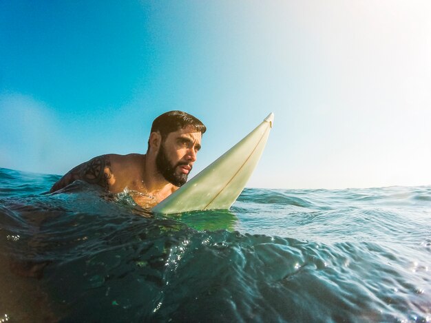 Homme debout avec planche de surf dans l&#39;eau bleue