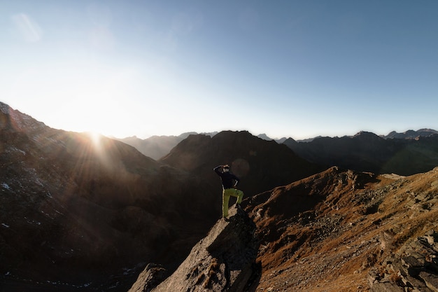 Homme debout sur un rocher au sommet d'une montagne face au soleil