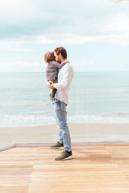 Photo gratuite homme debout tenant un enfant en bas âge au bord de mer