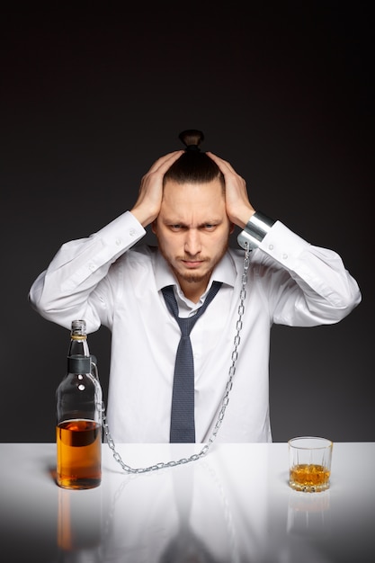 Photo gratuite homme déprimé assis avec une bouteille de whisky