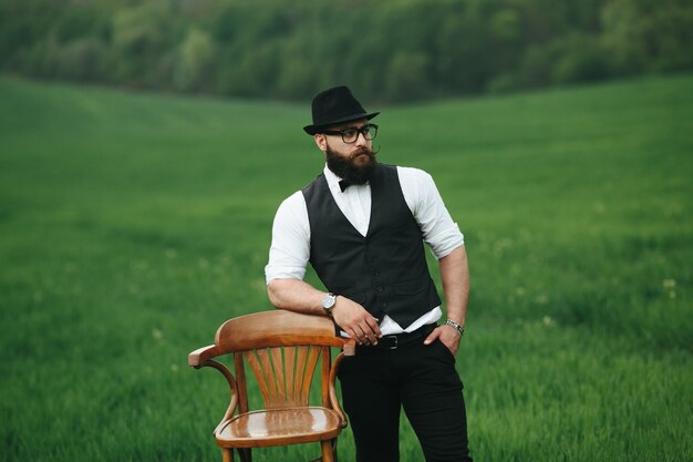 homme détendu avec le gilet et le chapeau à côté d&#39;une chaise en bois