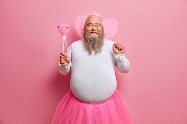 Un homme dodu positif s'amuse lors d'une soirée à thème, se sent comme une fée qui réalise les rêves, frissonne avec les enfants, a une barbe épaisse et un gros ventre