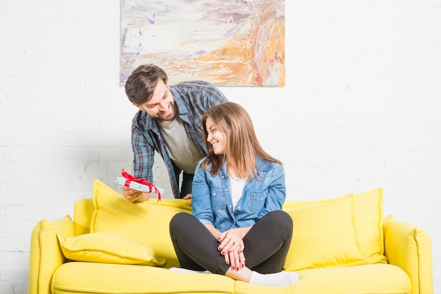 Homme donnant un cadeau à sa copine heureuse assise sur un canapé