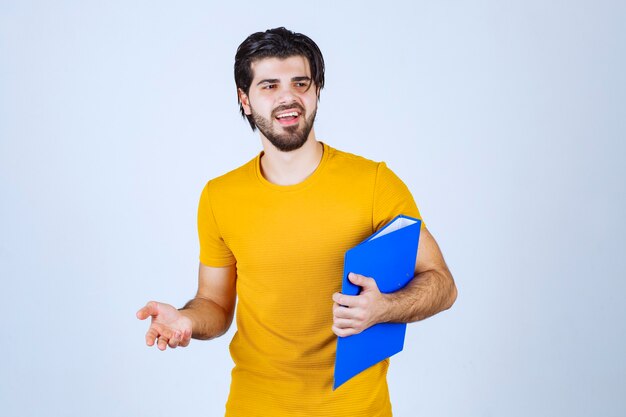 Homme avec un dossier bleu pointant son collègue sur le côté gauche et parlant avec émotions.