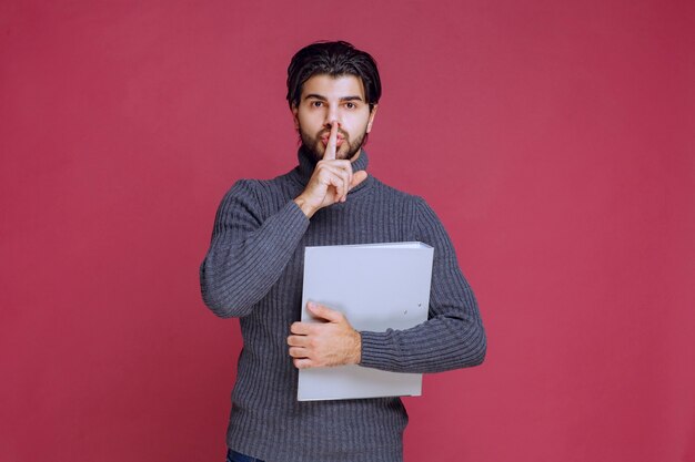 Homme avec dossier gris demandant le silence.