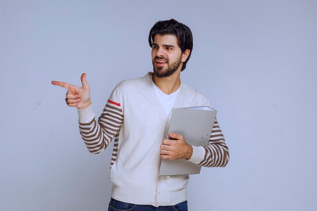 Homme avec un dossier de rapport et pointant quelqu'un sur la gauche.