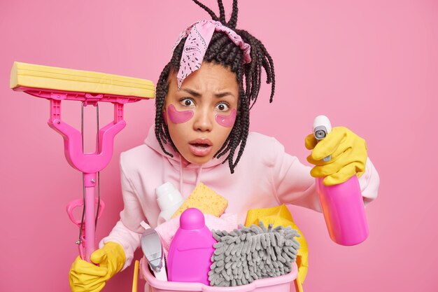 un homme avec des dreadlocks applique des tampons de collagène sous les yeux utilise un spray détergent et une vadrouille pour nettoyer le sol a l'air indigné