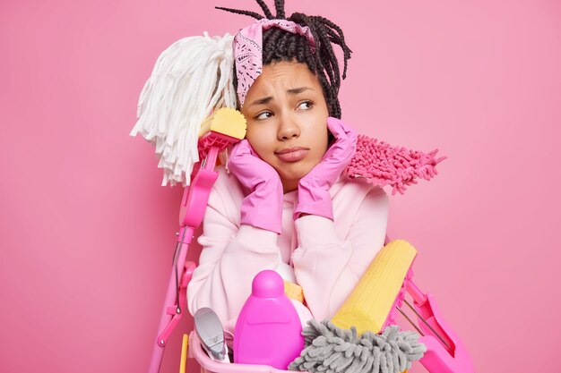 un homme avec des dreadlocks tient le menton entouré de produits de nettoyage tient près du bassin de lessive isolé sur rose