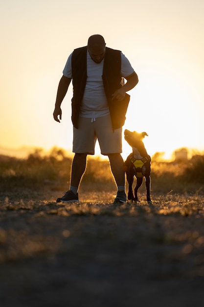 Homme dressant son chien à l'extérieur au coucher du soleil