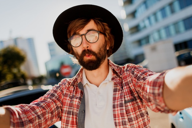 Homme drôle avec barbe faisant autoportrait par caméra alors qu'il voyageait dans une grande ville moderne d'Asie.