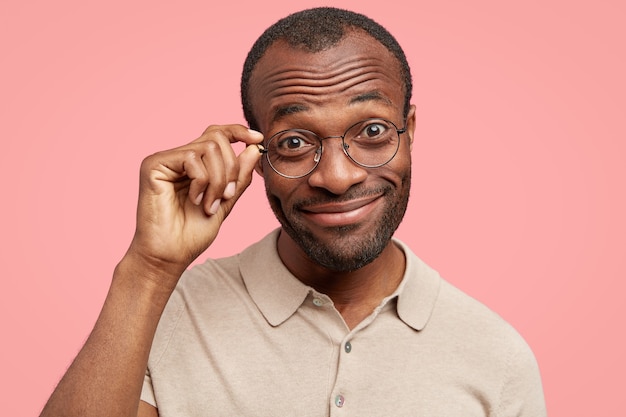 Photo gratuite un homme drôle et gai entend une histoire joyeuse intéressante de l'interlocuteur, regarde positivement à travers les lunettes