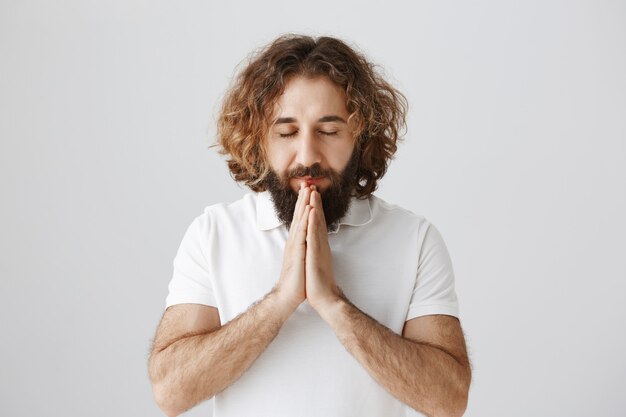 Un homme du Moyen-Orient plein d'espoir ferme les yeux et prie, se tient la main pour plaider