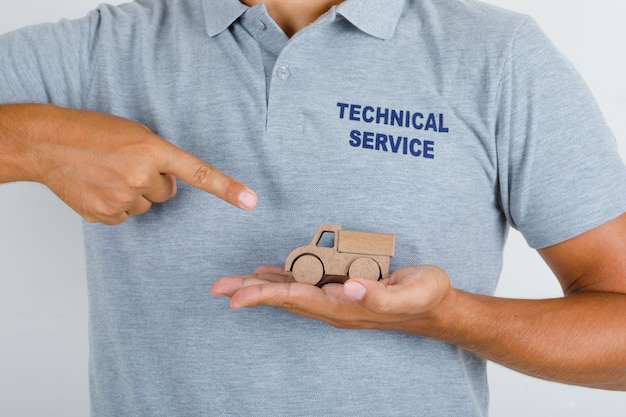 Homme du service technique montrant une petite voiture en bois en t-shirt gris