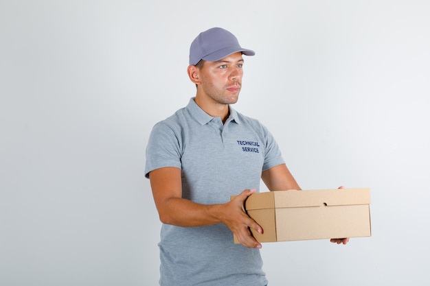 Homme du service technique tenant une boîte en carton en t-shirt gris avec capuchon