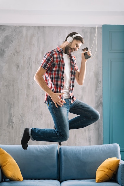 Photo gratuite homme écoutant de la musique et sautant sur le canapé