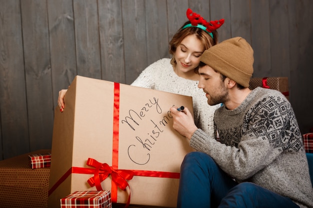 Homme écrit sur coffret cadeau joyeux Noël assis avec sa petite amie.