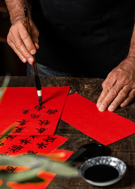 Homme écrivant des symboles chinois sur papier rouge