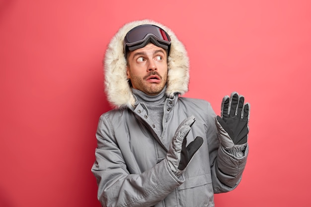 Un homme effrayé en hiver fait un geste défensif alors que quelque chose de lourd va lui tomber dessus porte une veste grise avec une capuche en fourrure et des lunettes de ski.