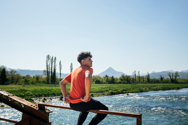 Homme élégant assis sur la rambarde métallique du pont au-dessus de la rivière