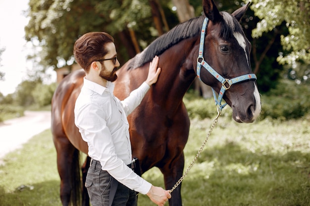 Homme élégant, debout à côté d'un cheval dans un ranch