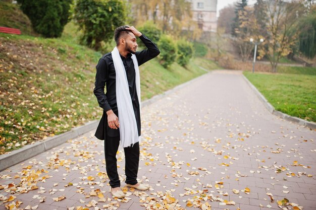 Homme élégant indien en vêtements traditionnels noirs avec foulard blanc posé en plein air contre l'automne jaune