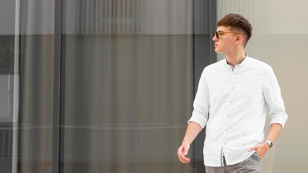 Homme élégant avec des lunettes de soleil posant à l'extérieur avec espace copie