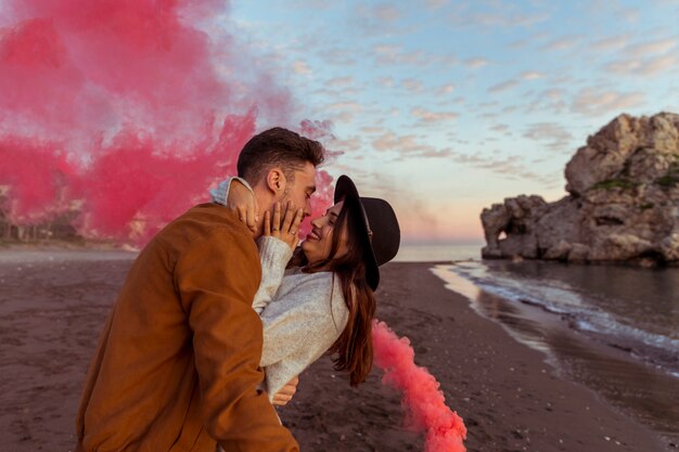 Homme embrassant une femme avec une bombe de fumée au bord de la mer