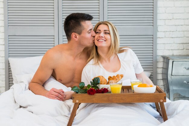 Homme embrasse une femme souriante au lit près du petit déjeuner à bord