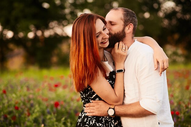 Homme embrasse sa femme tendre debout sur le champ plein de coquelicots