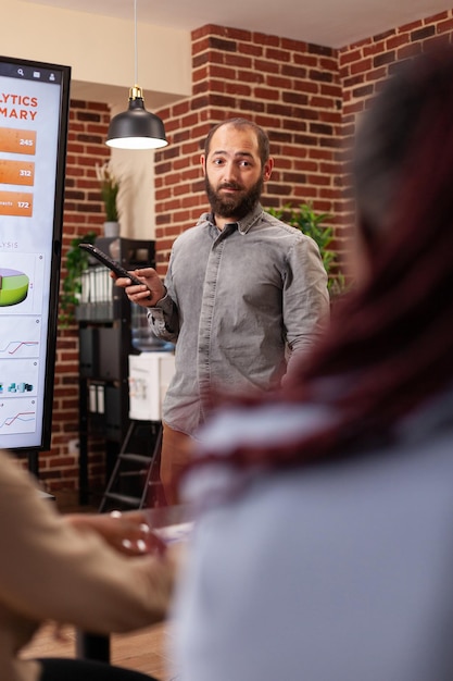 Homme entrepreneur pointant sur le moniteur expliquant les statistiques de gestion à l'équipe d'affaires travaillant à la présentation de l'entreprise dans le bureau de démarrage. Divers hommes d'affaires planifiant une présentation d'entreprise