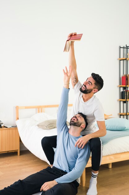 Homme essayant de prendre un livre de la main de son petit ami assis sur le lit