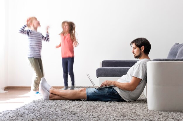 Homme essayant de travailler sur un ordinateur portable à la maison pendant que ses enfants courent partout