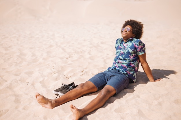 Homme ethnique se détendre pieds nus sur la plage de sable fin