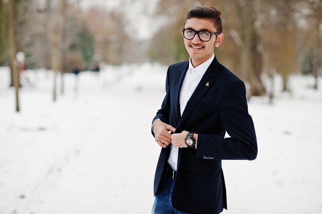 Homme étudiant indien élégant en costume et lunettes posé à la journée d'hiver en plein air