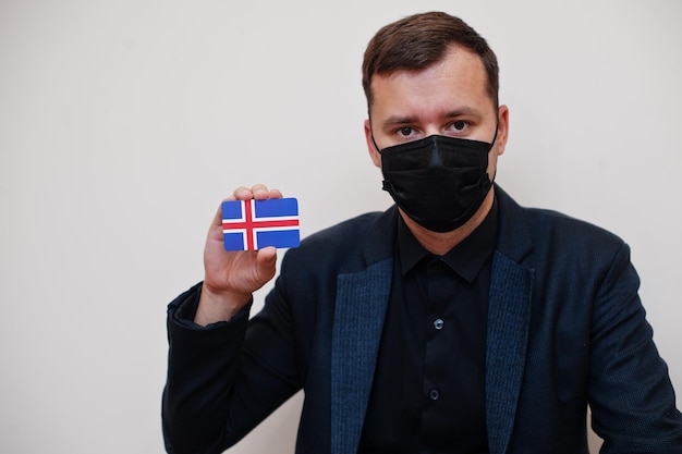 L'homme européen porte un masque formel noir et protège le visage tient la carte du drapeau de l'Islande isolée sur fond blanc Concept de pays Europe coronavirus Covid