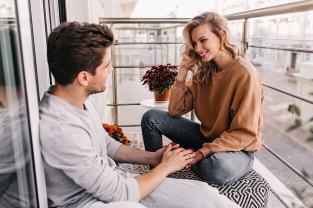 Homme européen touchant les mains de la petite amie. Femme souriante débonnaire parlant avec un ami au balcon.
