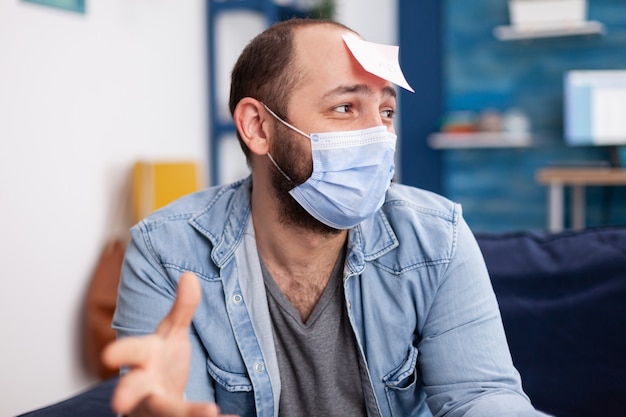 Homme excité jouant au jeu de nom avec des amis multiethniques portant un masque facial pour maintenir une distance sociale en raison de la pandémie sociale en s'amusant. Image conceptuelle.