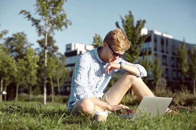 L'homme expressif est dans le parc avec son ordinateur portable