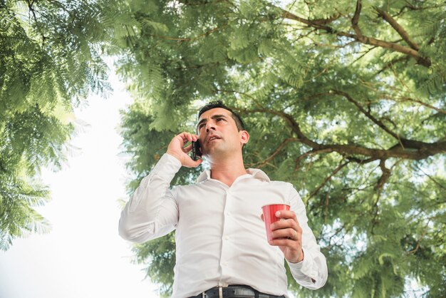 Photo gratuite homme faisant un appel téléphonique sous l'arbre