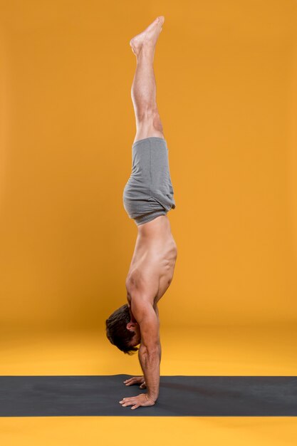 Homme faisant le poirier pose sur un tapis de yoga