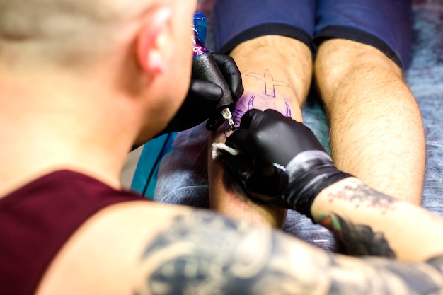 Homme faisant un tatouage avec une aiguille sur la jambe