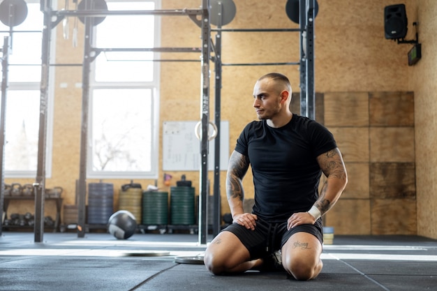 Homme fatigué assis au gymnase plein coup