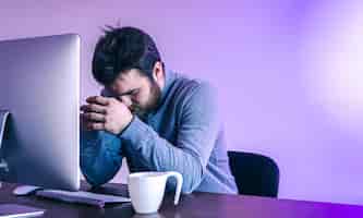 Photo gratuite un homme fatigué est assis devant un ordinateur avec une tasse d'éclairage de couleur café