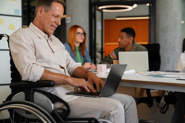 Photo gratuite homme en fauteuil roulant ayant un travail de bureau inclusif