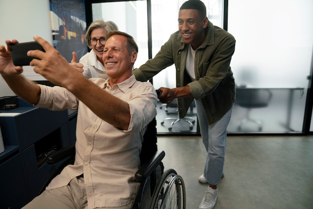 Homme en fauteuil roulant prenant un selfie sur son lieu de travail avec des collègues