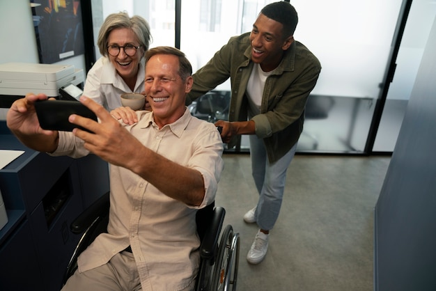 Homme en fauteuil roulant prenant un selfie sur son lieu de travail avec des collègues