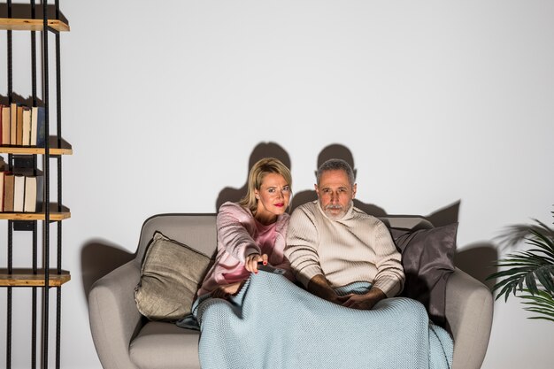 Homme et femme âgés avec télécommande de télévision changeant de chaîne et regardant la télévision sur un canapé